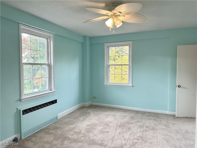 carpeted spare room featuring ceiling fan, a textured ceiling, plenty of natural light, and radiator heating unit