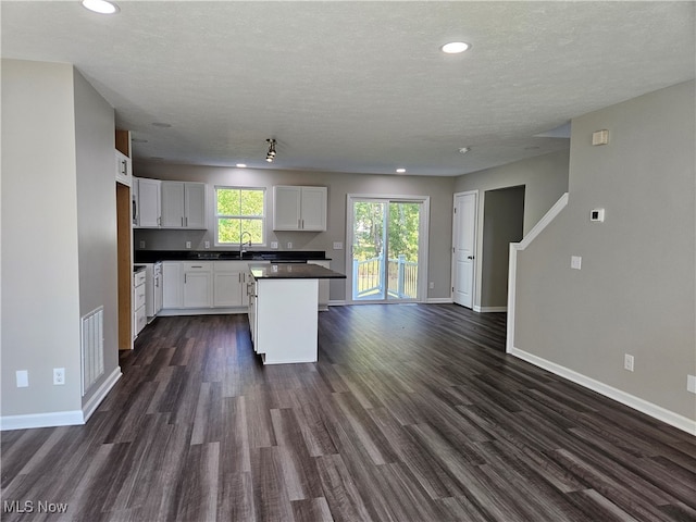 kitchen with white cabinets, a textured ceiling, dark hardwood / wood-style floors, sink, and a center island