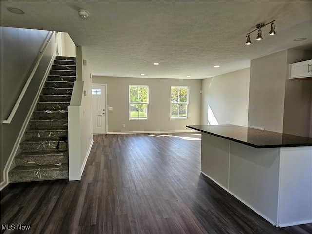 unfurnished living room featuring a textured ceiling, track lighting, and dark hardwood / wood-style floors