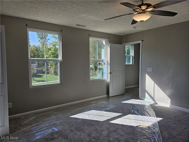 spare room featuring dark colored carpet, ceiling fan, a textured ceiling, and plenty of natural light