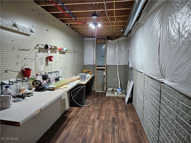 basement featuring electric panel, a workshop area, dark hardwood / wood-style flooring, and brick wall