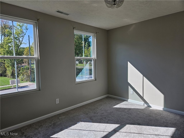 spare room with a healthy amount of sunlight, a textured ceiling, and dark carpet