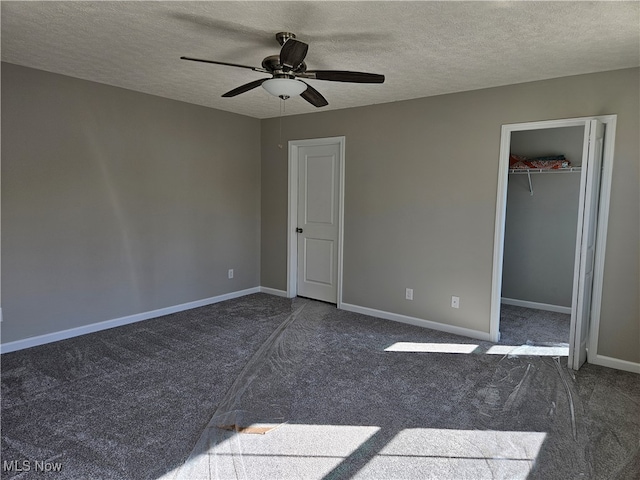 unfurnished bedroom featuring ceiling fan, a textured ceiling, a spacious closet, dark colored carpet, and a closet