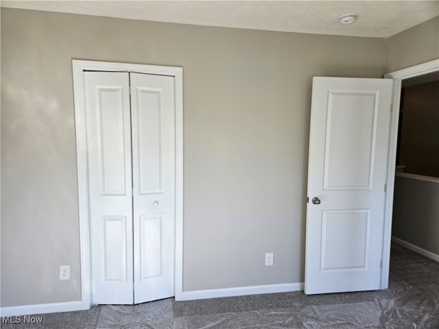 unfurnished bedroom with dark colored carpet, a textured ceiling, and a closet