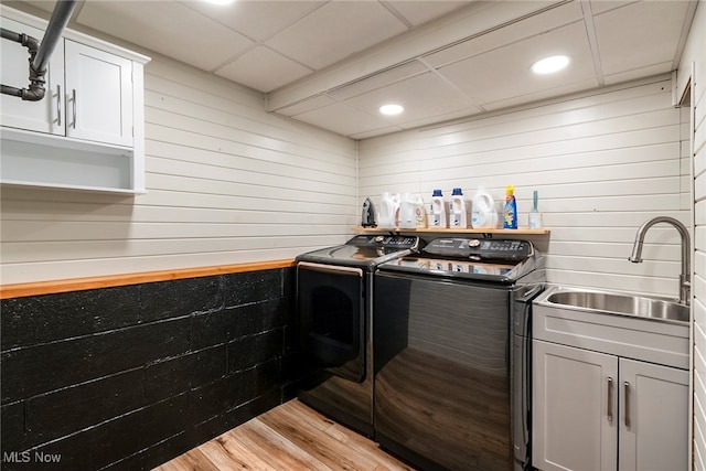 clothes washing area with sink, light wood-type flooring, cabinets, washer and dryer, and wood walls