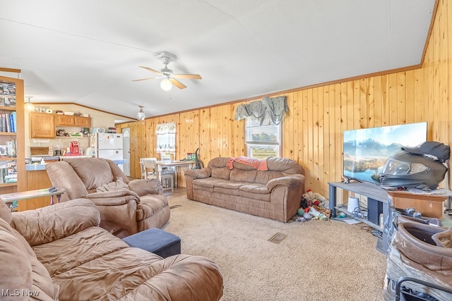 carpeted living room with lofted ceiling, wood walls, crown molding, and ceiling fan