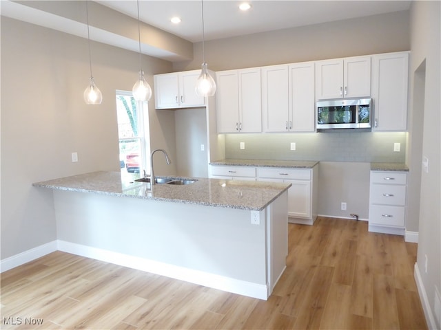 kitchen with sink, kitchen peninsula, white cabinetry, light hardwood / wood-style floors, and light stone counters