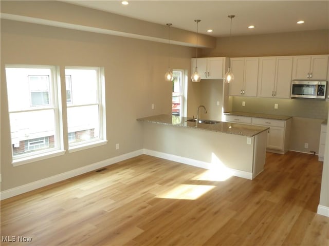 4424 W 53rd St, Cleveland, OH 44109 - kitchen with stainless steel microwave, a sink, a peninsula, white cabinetry, and pendant lighting