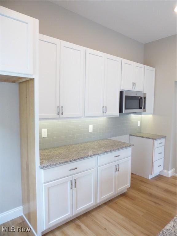 4424 W 53rd St, Cleveland, OH 44109 - kitchen featuring stainless steel microwave, white cabinets, tasteful backsplash, light wood-style flooring, and light stone counters