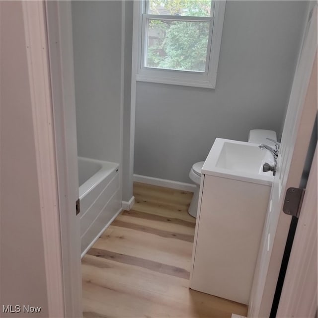 bathroom featuring vanity, toilet, wood-type flooring, and a bath