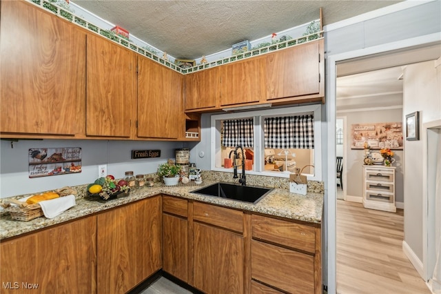 kitchen with sink, light stone countertops, a textured ceiling, and light hardwood / wood-style floors