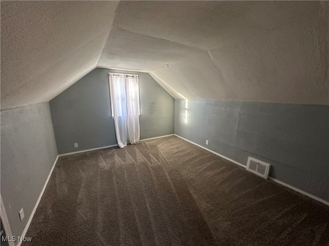 additional living space with dark carpet, lofted ceiling, and a textured ceiling