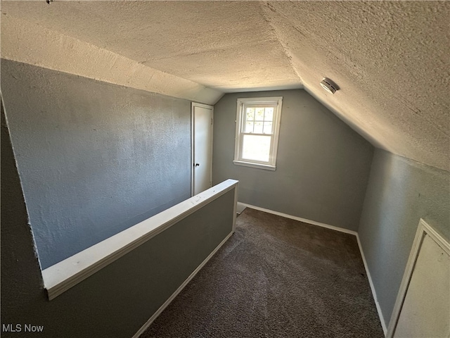 additional living space featuring lofted ceiling, a textured ceiling, and dark carpet