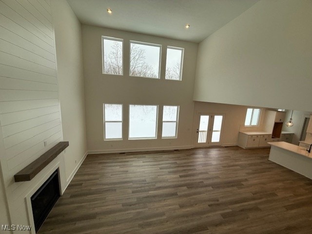 unfurnished living room featuring dark wood-type flooring and a towering ceiling