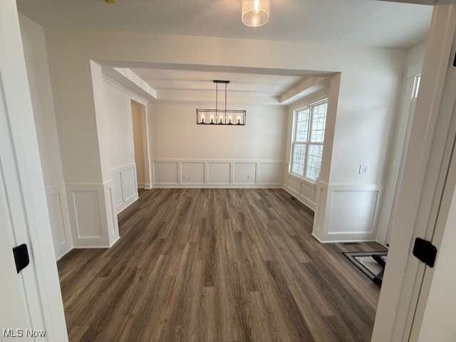 unfurnished dining area with a textured ceiling, dark hardwood / wood-style flooring, and a raised ceiling