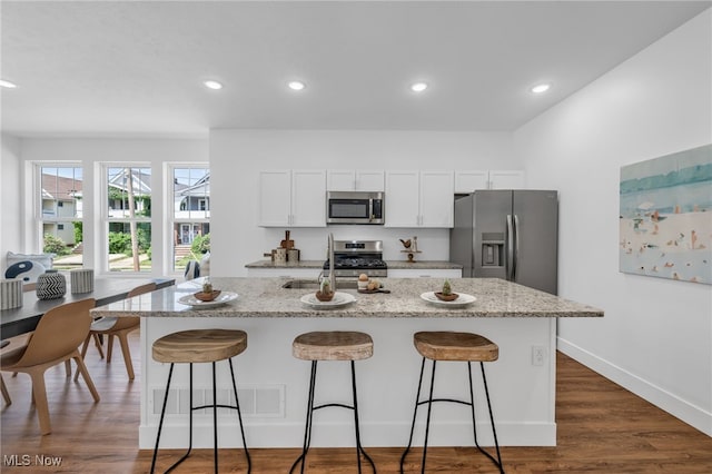 kitchen with a kitchen breakfast bar, a kitchen island with sink, stainless steel appliances, and dark wood-type flooring