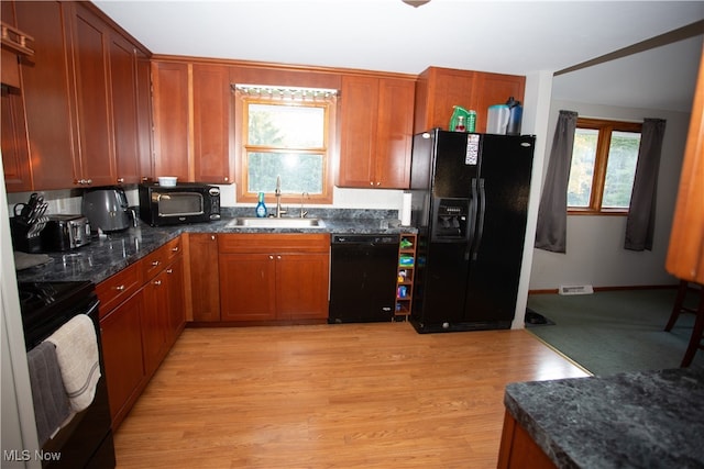 kitchen with dark stone countertops, sink, black appliances, and light wood-type flooring