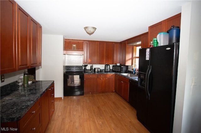 kitchen with sink, light hardwood / wood-style floors, dark stone countertops, and black appliances