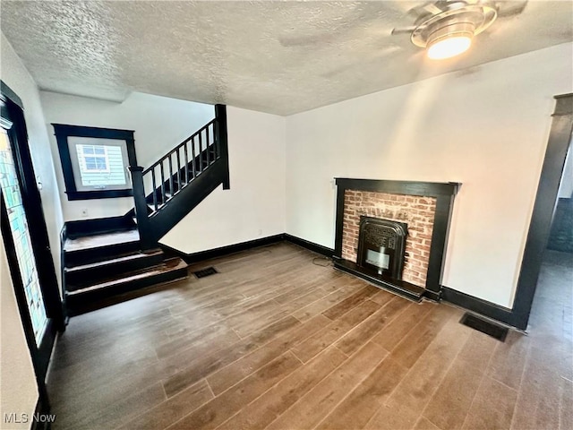 unfurnished living room featuring wood-type flooring, a textured ceiling, and a brick fireplace