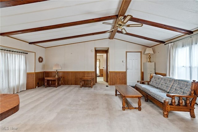 living room featuring vaulted ceiling with beams, ceiling fan, light colored carpet, and wood walls