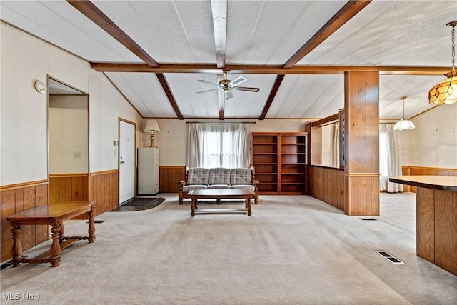 carpeted living room featuring lofted ceiling with beams, ceiling fan, a textured ceiling, and wooden walls