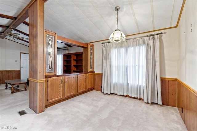 unfurnished dining area with light carpet, wooden walls, ceiling fan, and vaulted ceiling