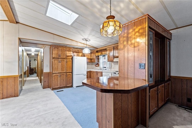 kitchen featuring carpet flooring, vaulted ceiling with skylight, decorative light fixtures, white fridge, and kitchen peninsula