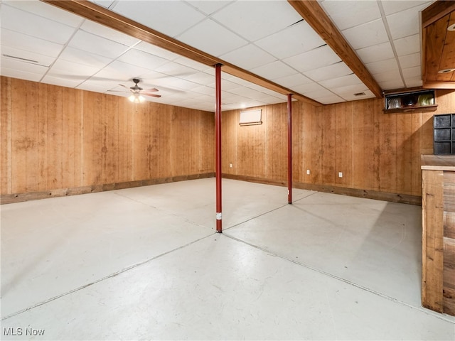 basement featuring a drop ceiling, wood walls, and ceiling fan