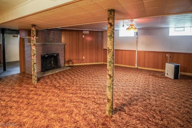 basement featuring wood walls, carpet floors, and a brick fireplace