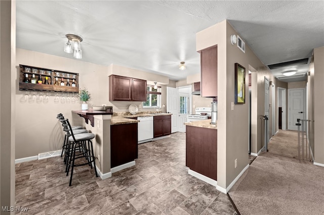 kitchen featuring light carpet, kitchen peninsula, a textured ceiling, a kitchen bar, and white appliances