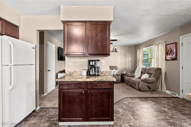 kitchen with carpet, light stone countertops, dark brown cabinetry, white fridge, and a textured ceiling