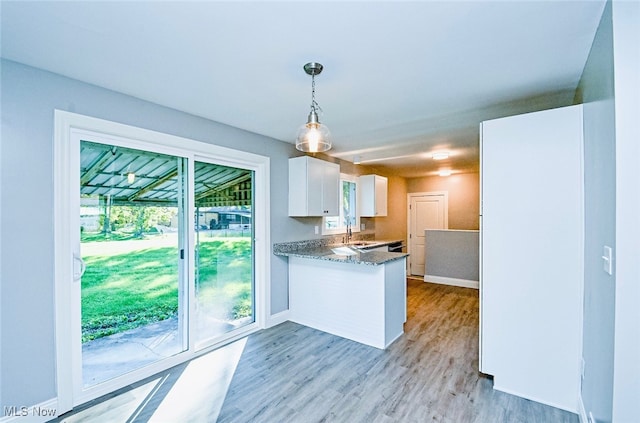 kitchen featuring light wood-type flooring, kitchen peninsula, hanging light fixtures, white cabinets, and dark stone countertops