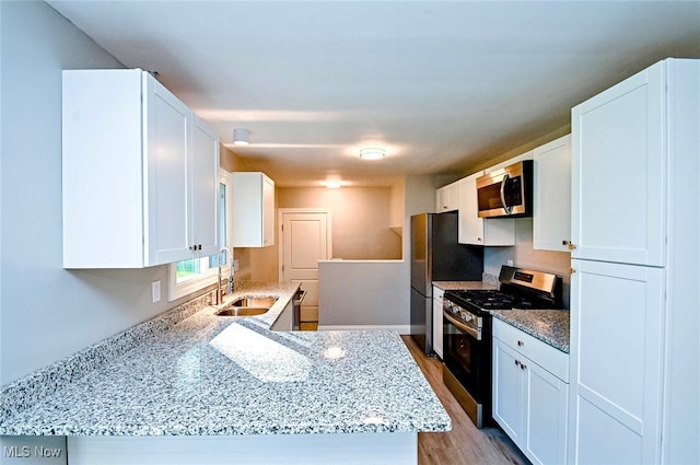 kitchen with white cabinets, light stone counters, sink, light hardwood / wood-style floors, and stainless steel appliances