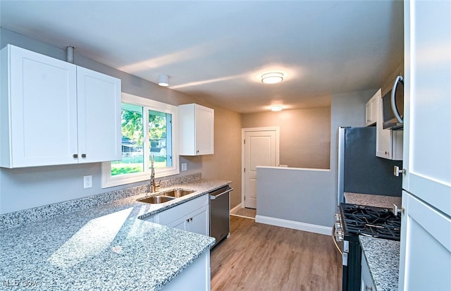 kitchen with stainless steel appliances, sink, light stone countertops, white cabinetry, and light hardwood / wood-style floors