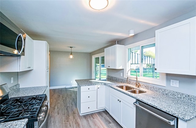 kitchen with kitchen peninsula, stainless steel appliances, sink, pendant lighting, and white cabinets