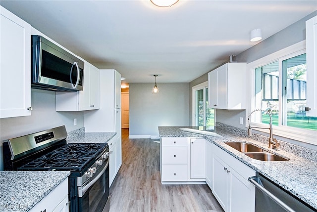 kitchen featuring white cabinets, appliances with stainless steel finishes, light wood-type flooring, pendant lighting, and sink