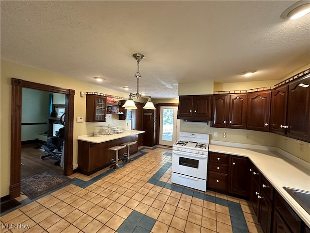 kitchen featuring light tile patterned floors, a textured ceiling, pendant lighting, white range with gas stovetop, and dark brown cabinetry