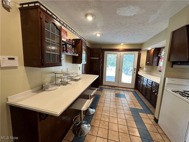 kitchen with dark brown cabinets, a textured ceiling, a kitchen breakfast bar, white gas range, and light tile patterned floors