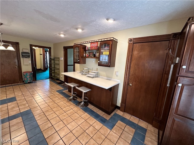 kitchen with a kitchen breakfast bar, kitchen peninsula, hanging light fixtures, light tile patterned floors, and a textured ceiling