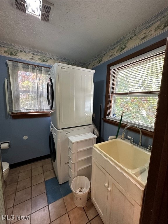 laundry room with sink, stacked washer / drying machine, a textured ceiling, and light tile patterned floors