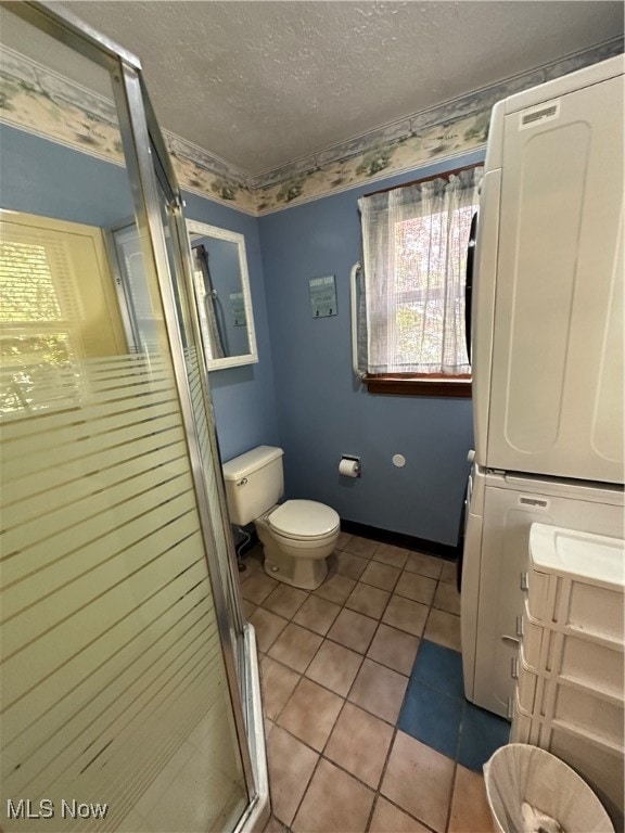 bathroom with a shower with door, tile patterned floors, stacked washer and dryer, toilet, and vanity