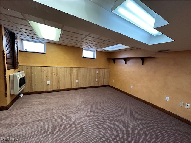 basement featuring wood walls, a paneled ceiling, heating unit, and carpet