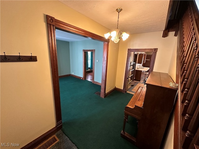 hallway with a notable chandelier, a textured ceiling, and dark colored carpet