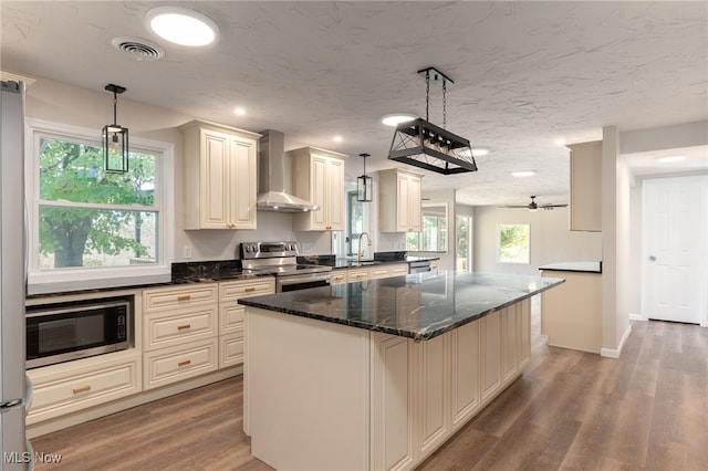 kitchen featuring hanging light fixtures, wall chimney exhaust hood, stainless steel appliances, and wood-type flooring