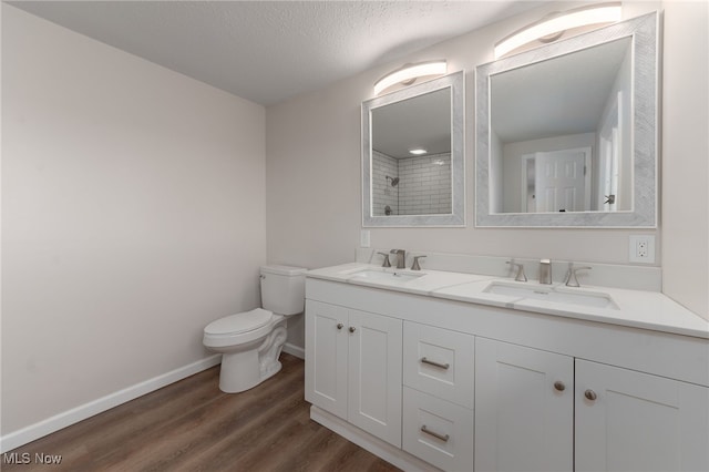 bathroom with vanity, a textured ceiling, tiled shower, wood-type flooring, and toilet