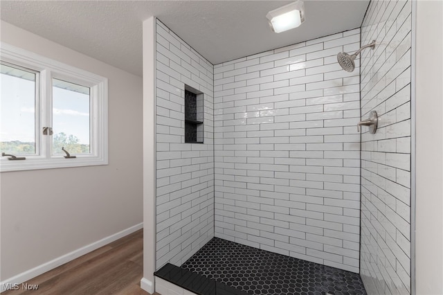 bathroom with a textured ceiling, wood-type flooring, and tiled shower