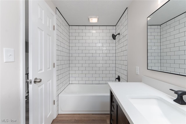 bathroom featuring hardwood / wood-style floors, vanity, a textured ceiling, and tiled shower / bath