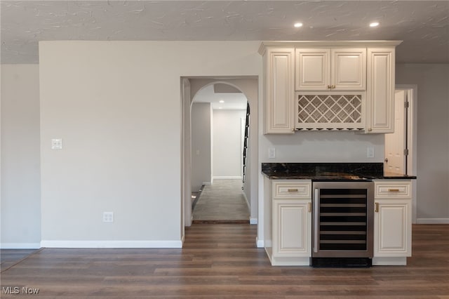 bar with dark stone counters, white cabinetry, dark wood-type flooring, and beverage cooler