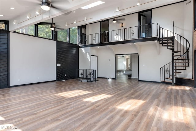 unfurnished living room with a towering ceiling, light hardwood / wood-style flooring, and ceiling fan