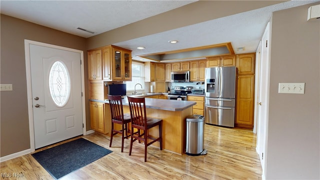 kitchen with a kitchen bar, kitchen peninsula, appliances with stainless steel finishes, and light hardwood / wood-style flooring